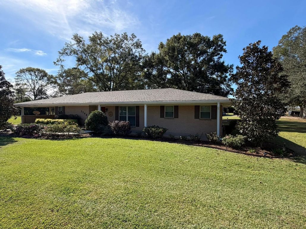 Single-story house with a front lawn, trees, and clear blue sky