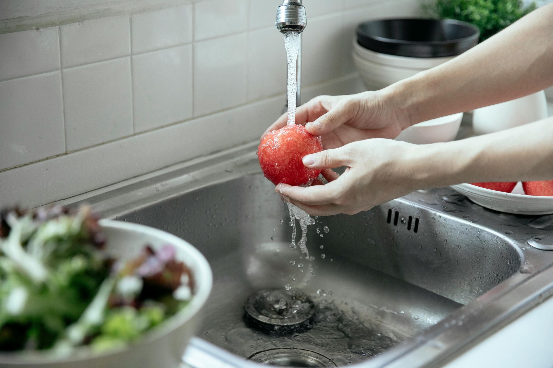 A person is washing an apple in a kitchen sink with clean water