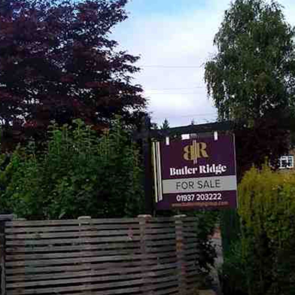 A purple for sale sign is sitting on top of a wooden fence.