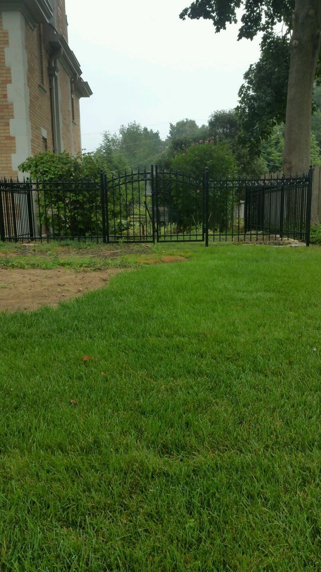 A Lush Green Lawn With A Fence And A Building In The Background – Mishawaka IN - Milestone Fence