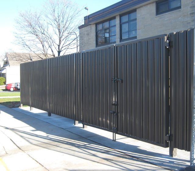 A Black Fence With A Brick Building In The Background – Mishawaka IN - Milestone Fence