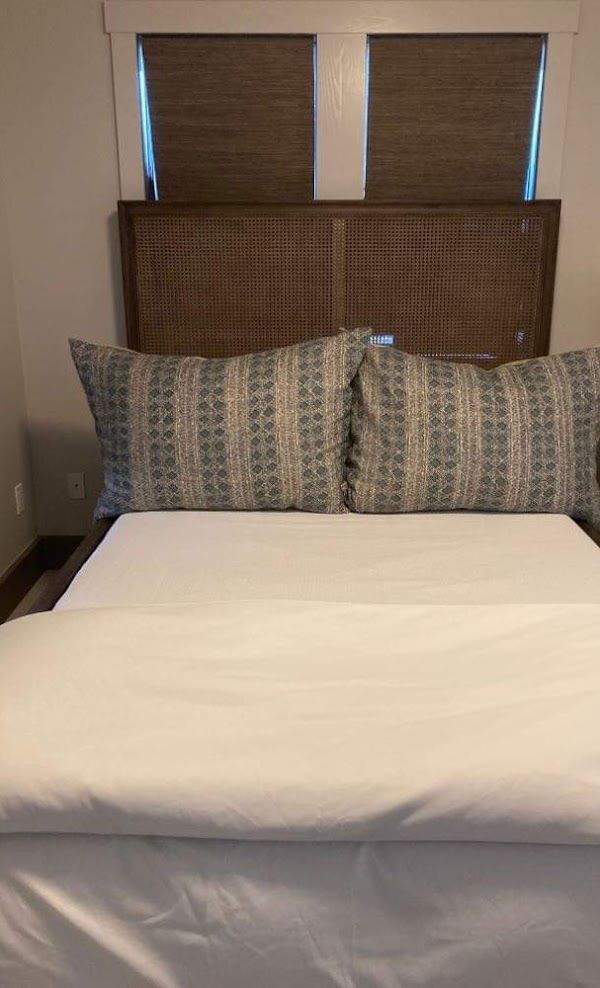 A bed with white sheets and pillows in a bedroom with a window.