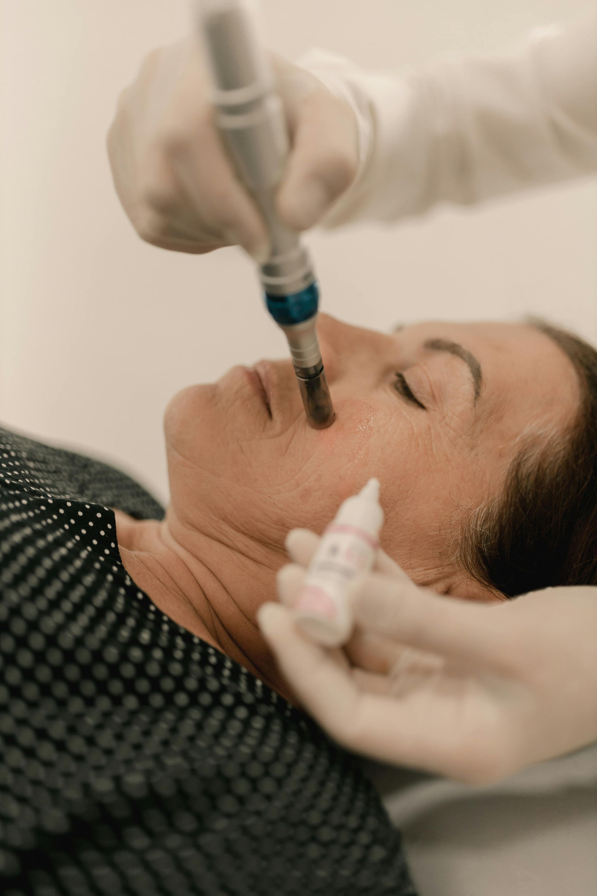 Cosmetologist tattooing a client’s eyebrow with a handheld machine in a salon