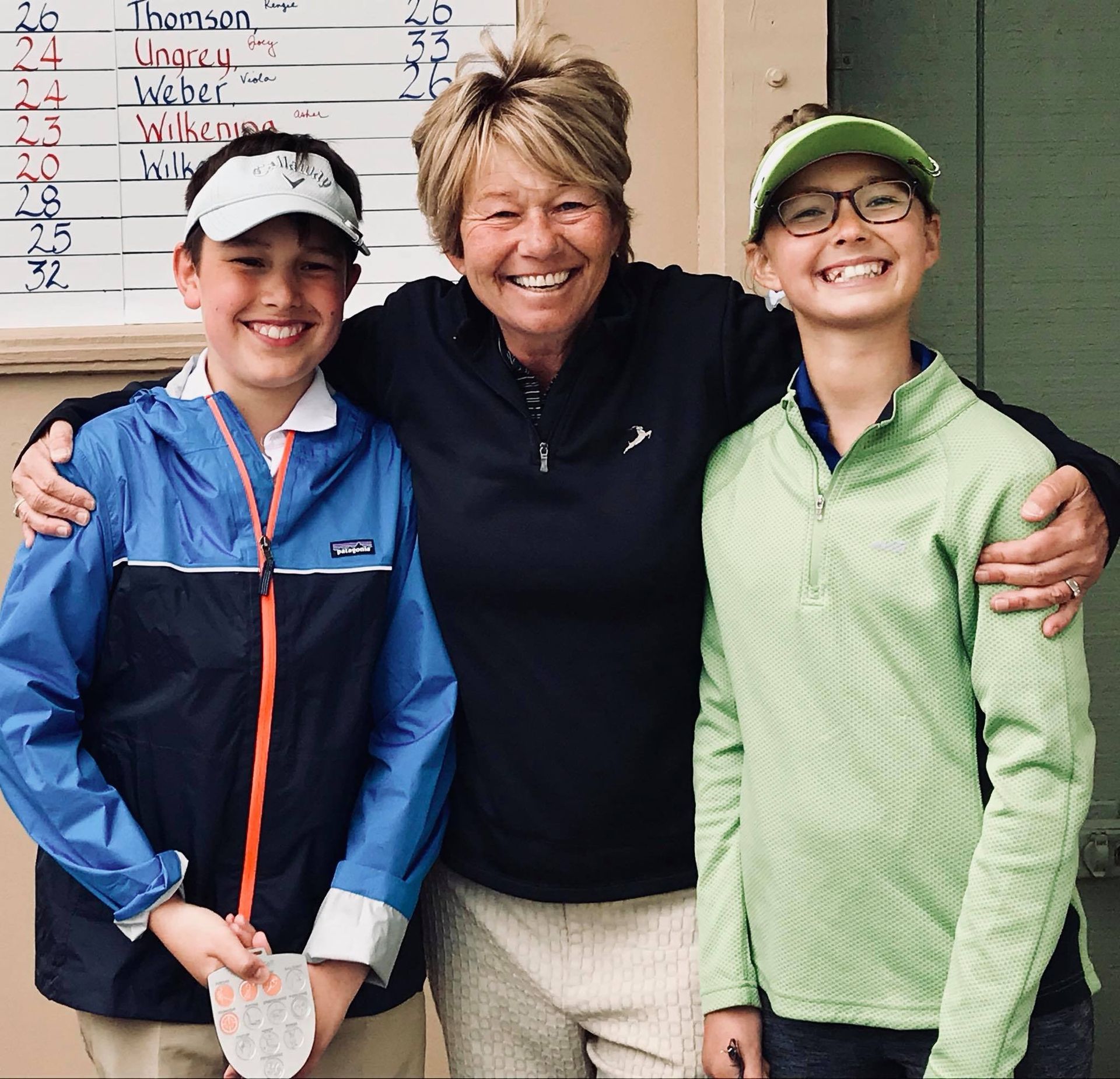 A woman and two children pose for a picture in front of a scoreboard