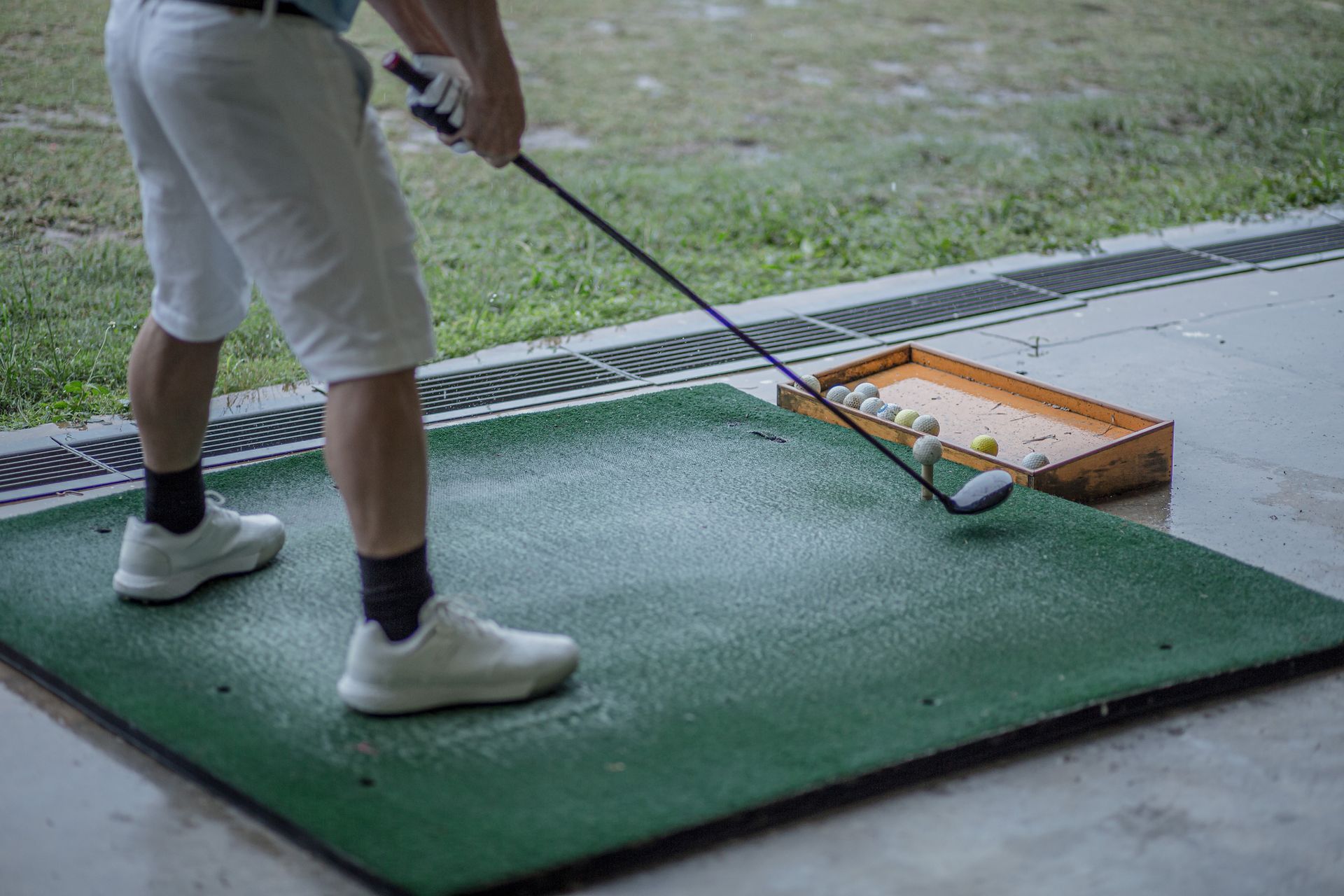 A man is standing on a golf mat holding a golf club.