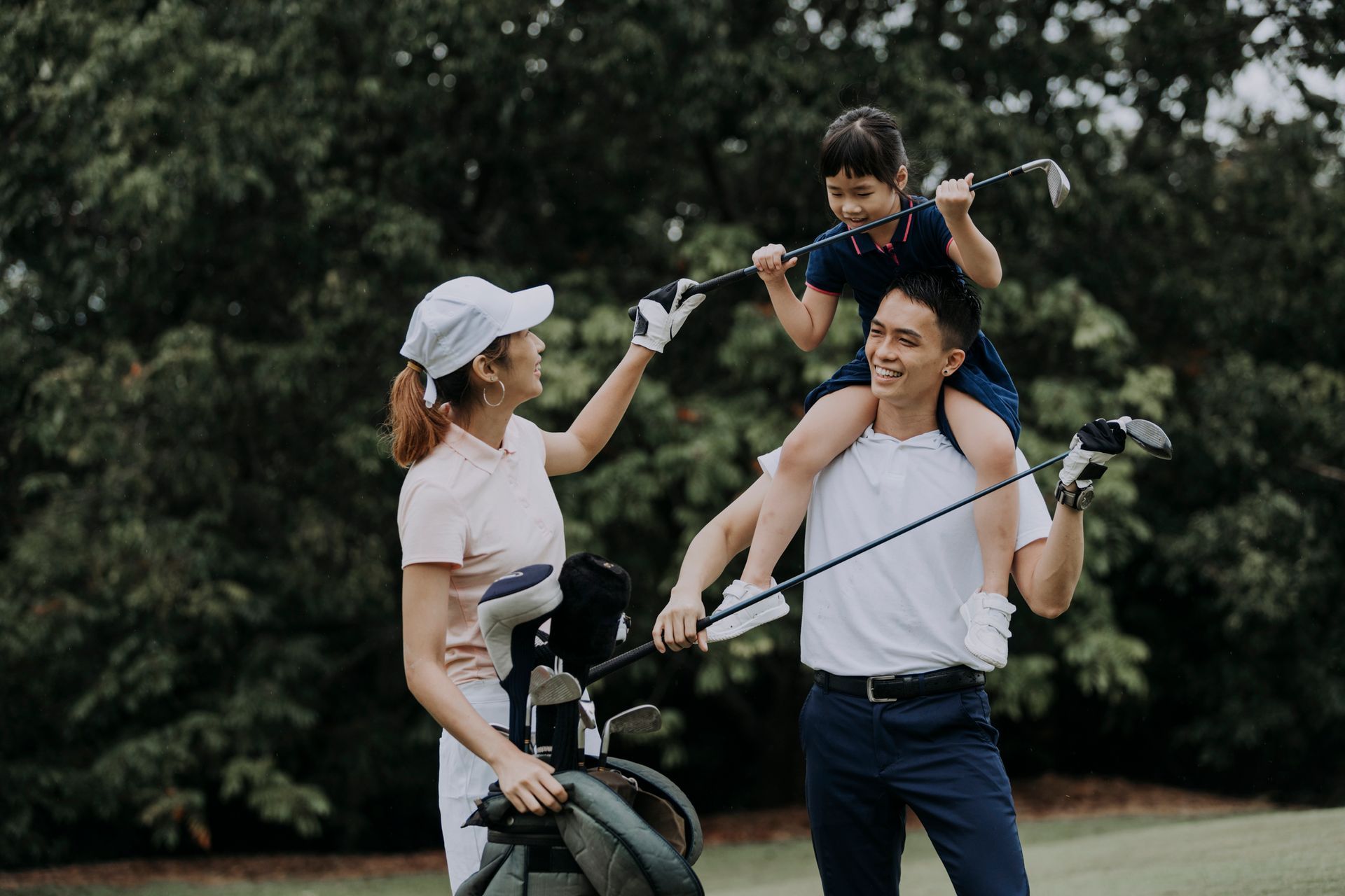 A man is carrying a child on his shoulders while holding a golf club.