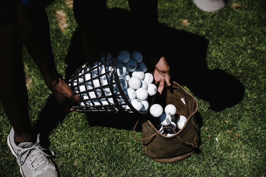 A person is holding a basket of golf balls on a golf course.