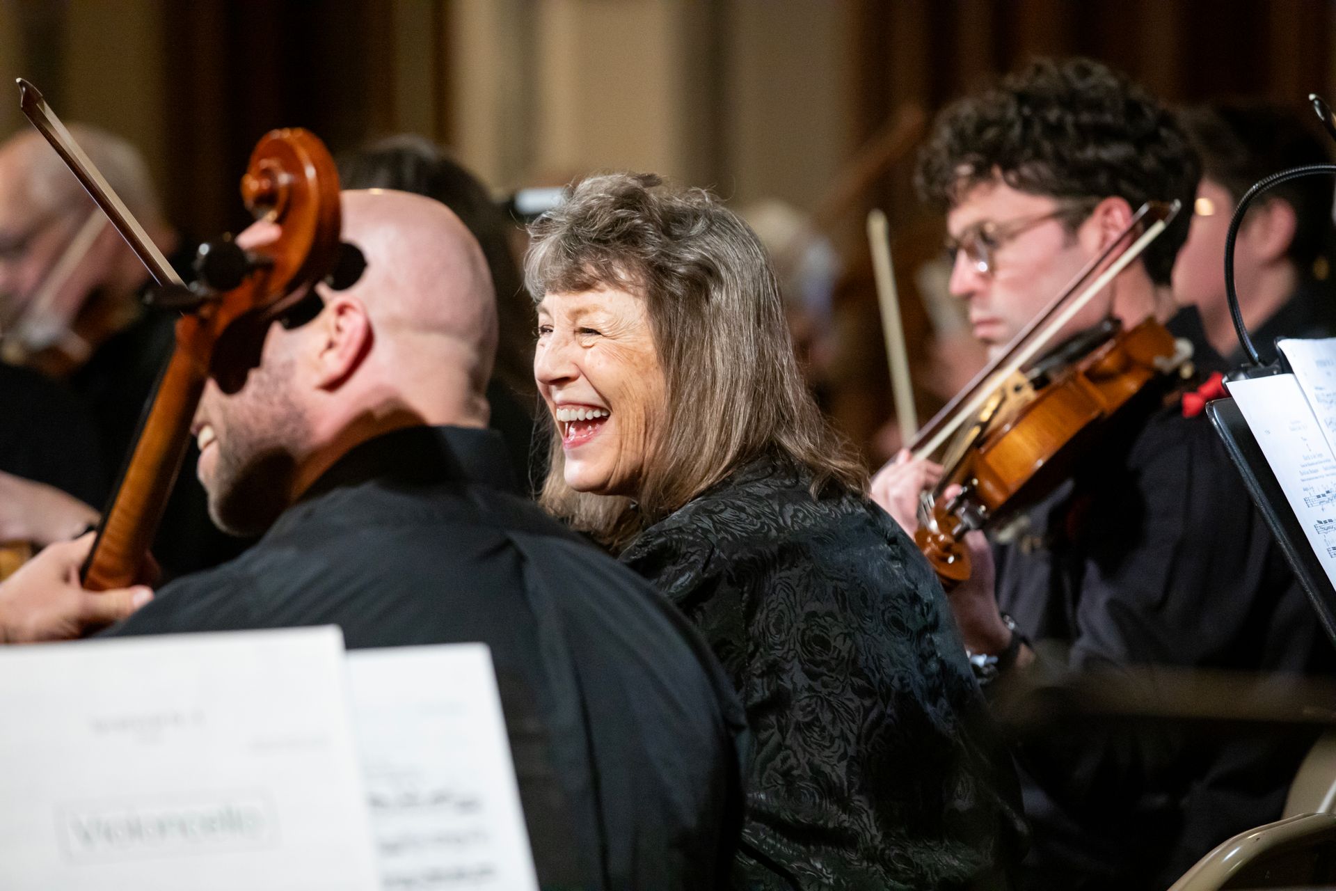 A woman is laughing while playing a violin in an orchestra.