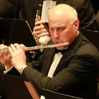 A man in a tuxedo is playing a flute in an orchestra