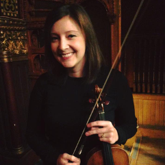 A woman in a black shirt is smiling while holding a violin