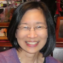 A woman wearing glasses and a purple sweater smiles for the camera