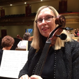 A woman is playing a cello in a concert hall.