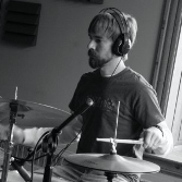 A man wearing headphones is playing drums in a black and white photo.