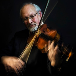 A man with glasses and a beard is playing a violin