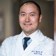 A man in a white coat and tie is smiling for the camera.