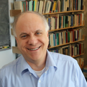 A man in a blue shirt is smiling in front of a bookshelf