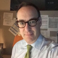 A man wearing glasses and a tie takes a selfie