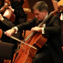 A man in a suit is playing a cello in an orchestra