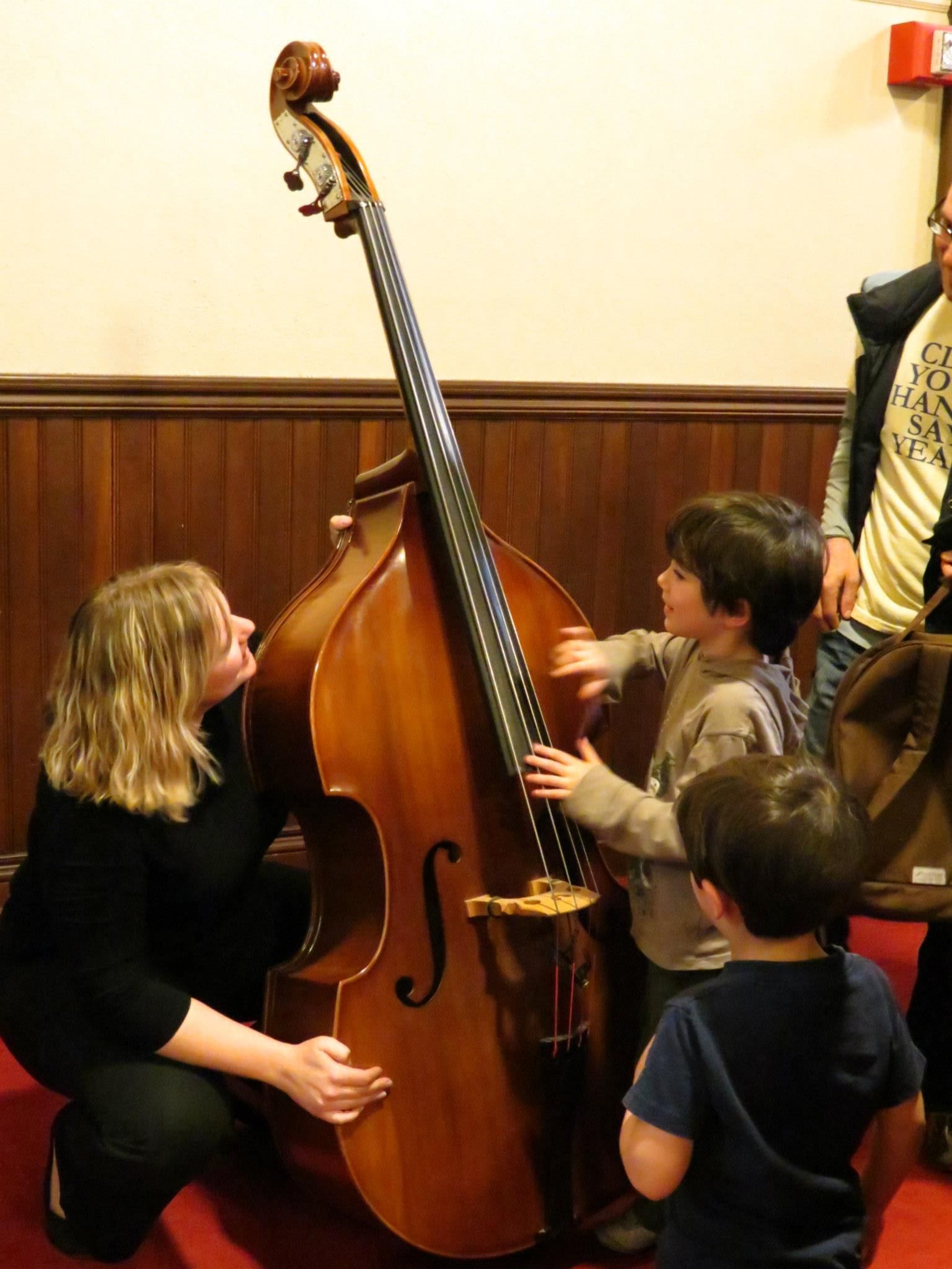 A woman is kneeling down next to a child playing a double bass