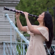A woman in a dress is playing a clarinet in a park.