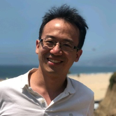 A man wearing glasses and a white shirt is smiling for the camera.