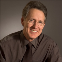 A man wearing glasses and a brown shirt smiles for the camera