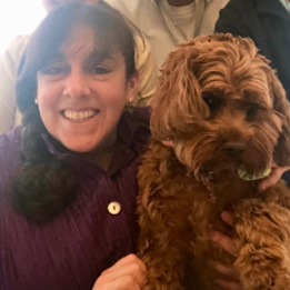 A woman in a purple shirt is holding a brown dog