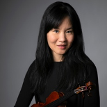 A woman in a black shirt is holding a violin.