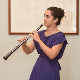 A woman in a purple dress is playing a clarinet.
