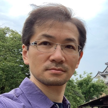 A man wearing glasses and a purple shirt is taking a selfie.