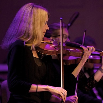 A woman is playing a violin in front of a purple light.