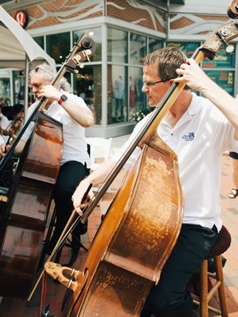 A man is playing a double bass in a band while sitting on a stool.