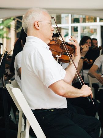 A man in a white shirt is playing a violin in an orchestra.