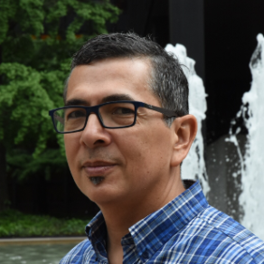 A man wearing glasses is standing in front of a fountain