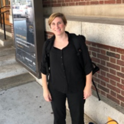 A woman in a black shirt is standing in front of a brick wall