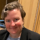 A woman in a black jacket is smiling for the camera.