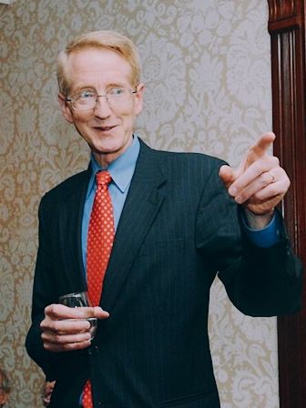 A man in a suit and tie is holding a glass and pointing