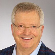 A man wearing glasses and a blue jacket is smiling for the camera