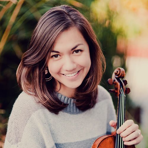 A woman is holding a violin and smiling for the camera