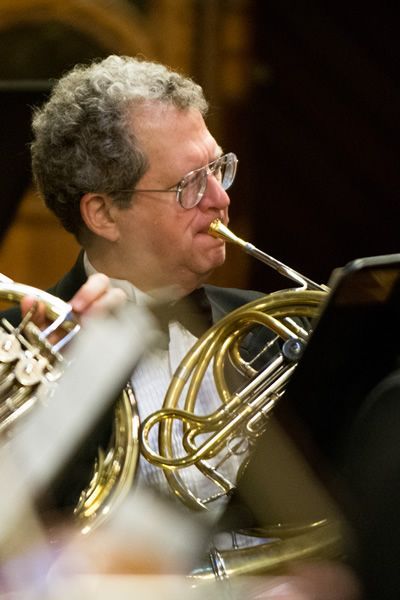 A man is playing a french horn in an orchestra