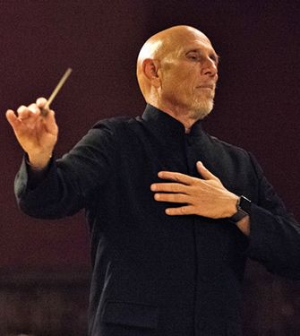 A bald man in a black jacket is holding a baton