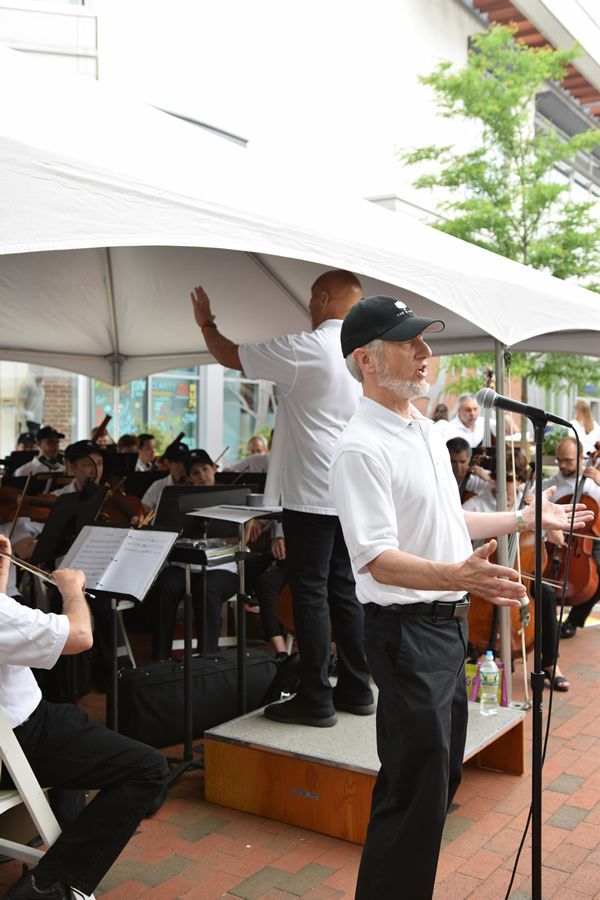 A man is standing in front of a microphone in front of an orchestra.