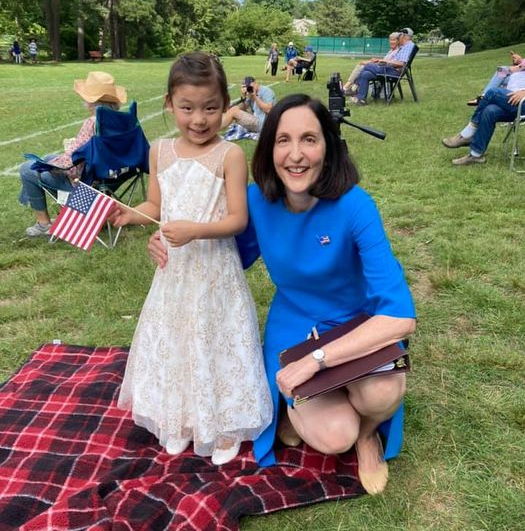 A woman is kneeling next to a little girl who is holding an american flag.