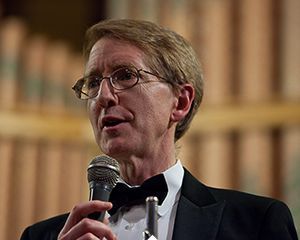 A man in a tuxedo and bow tie is holding a microphone.