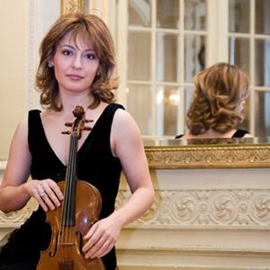 A woman in a black dress is holding a violin in front of a mirror