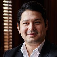 A man in a suit and white shirt is smiling in front of a window.
