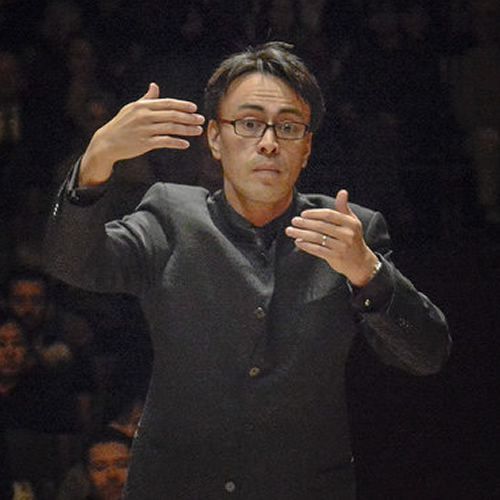 A man in a suit and glasses is standing in front of a crowd.