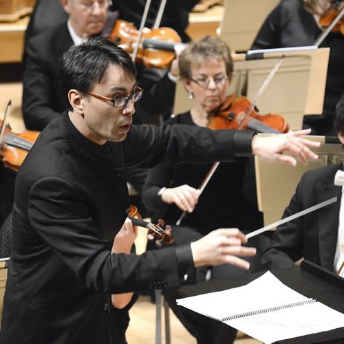 A man in a black suit is directing an orchestra