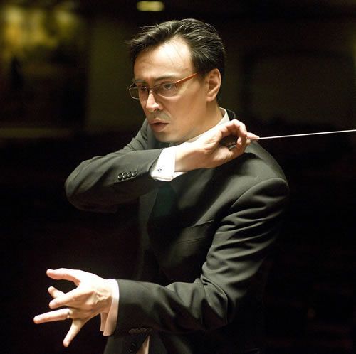 A man in a suit and glasses is holding a baton
