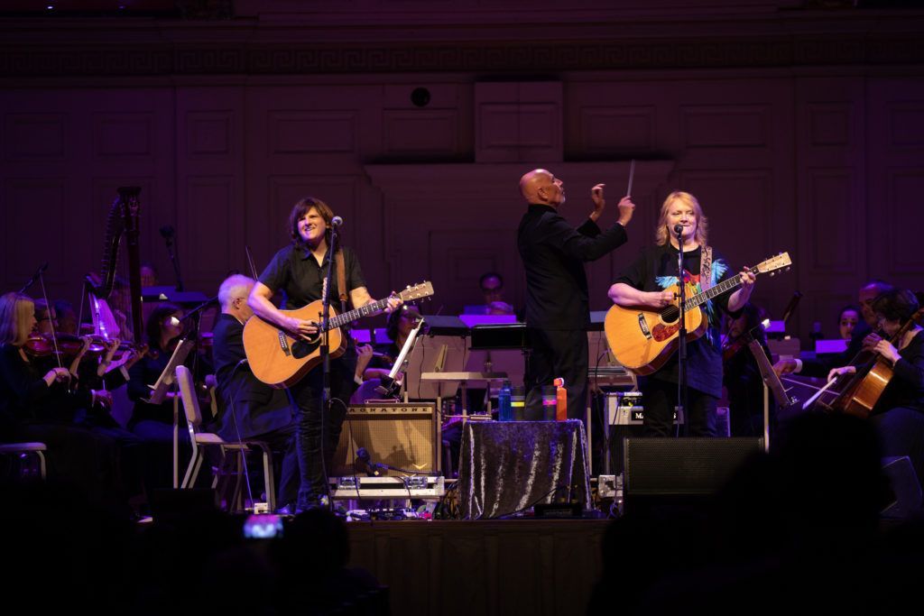 A group of people are playing guitars on a stage in front of an orchestra.